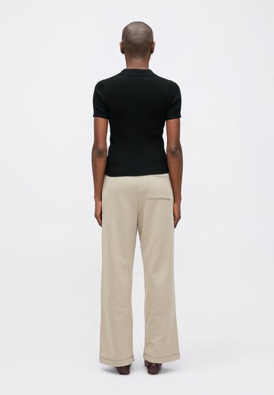 Melnas, ribotas īso piedurkņu blūze apvienota ar bēša platām biksēm. Blūzei ir pieguļošs siluets, savukārt biksēm ir aizmugurējā kabata.