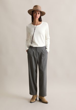 Witte lange mouwen top, grijs geruit hooggewaisted broek, en een bruine hoed met brede rand en een donker koorddetail. Lichtbruine enkellaarsjes met hak.