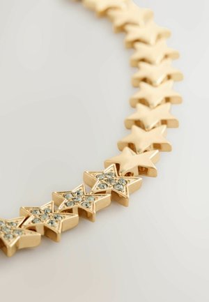 Zelta zvaigzne forma aproce ar dažām zvaigznēm, kuras rotā mazi caurspīdīgi rhinestone akmeņi uz gaiša fona.