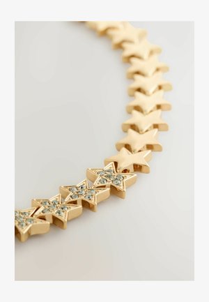 Zelta zvaigzne forma aproce ar dažām zvaigznēm, kuras rotā mazi caurspīdīgi rhinestone akmeņi uz gaiša fona.