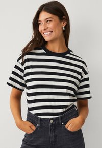 T-shirt à manches courtes noir et blanc rayé avec un col rond, associé à un jean en denim noir taille haute. En matière de coton, coupe décontractée.