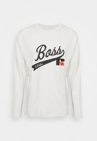 Vit långärmad t-shirt med svart "Boss"-logotyp, röd accent och en böjd svart bannerdesign. Bomullstyg med en mjuk textur.