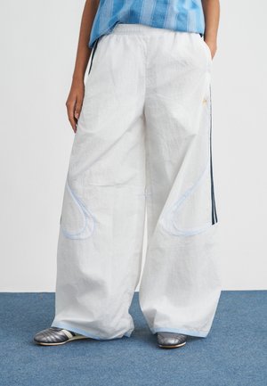 Pantaloni bianchi a gamba larga con cuciture azzurro chiaro e strisce laterali, realizzati in tessuto strutturato. Abbinati a scarpe metalliche argentate.