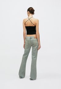 Must ribihaalis lühike top, millel on ristuvad õlapaelad, kombineeritud heledate roheliste paagutatud teksadega, millel on ristkülikukujuline tagumine plaastritükk ja kaks tagataskut.