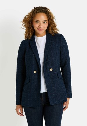 Blazer de color marino con textura y patrón tejido, diseño de doble botonadura, botones dorados y dos bolsillos frontales, llevado sobre una camiseta blanca.