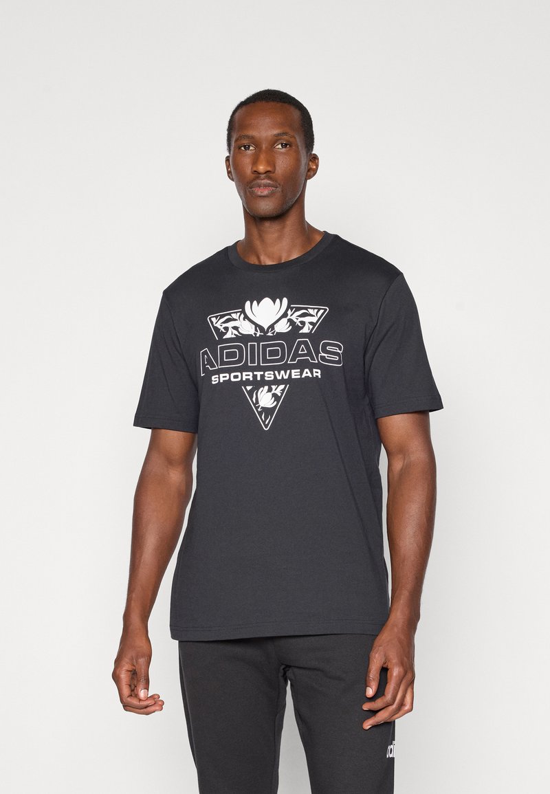 Juodas marškinėliai su dideliu baltu Adidas logotipu ir gėlių dizainu priekyje, klasikiniu apvaliu iškirpimu ir trumpomis rankovėmis.