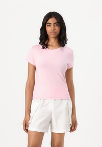 Tricou sportiv scurt, roz, cu mâneci scurte și decolteu rotund. Are un mic logo alb pe piept. Este asortat cu pantaloni scurți cargo albi.