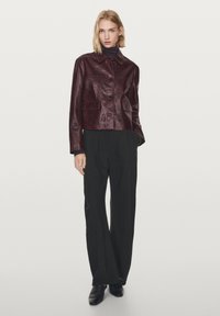 Vinrød lædercropped jakke med krave, knaplukning foran og to påsyede lommer, kombineret med sorte bukser med vide ben.