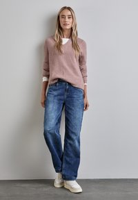 Ljusrosa, strukturerad tröja lager på lager över en vit topp, parat med mörkblå, löst sittande jeans och vita sneakers. Enkelt mönster med V-ringning.