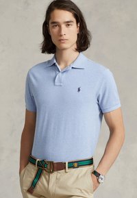Polo shirt de culoare albastră deschisă, din bumbac, cu colier clasic, mâneci scurte și un logo mic, întunecat. Purtați cu pantaloni khaki și o curea cu un model.