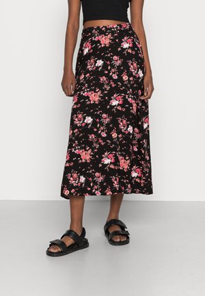 Persoon draagt een zwarte midirok met roze en witte bloemenprint, een zwart crop-topje en zwarte sandalen met twee banden en gespen.
