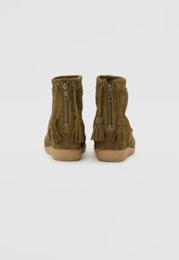Bottines en suede vert olive avec zips à l'arrière et des pampilles décoratives, dotées d'une semelle en caoutchouc texturé de couleur beige.