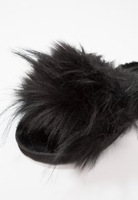Black slipper featuring a fluffy, textured upper with long strands of faux fur, a flat sole, and a smooth, dark lining.