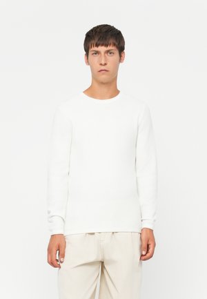 Witte, lange mouwen textuurtrui met een ronde hals, gecombineerd met lichtgekleurde, losvallende broek. Eenvoudig ontwerp, zonder zichtbare patronen of accenten.