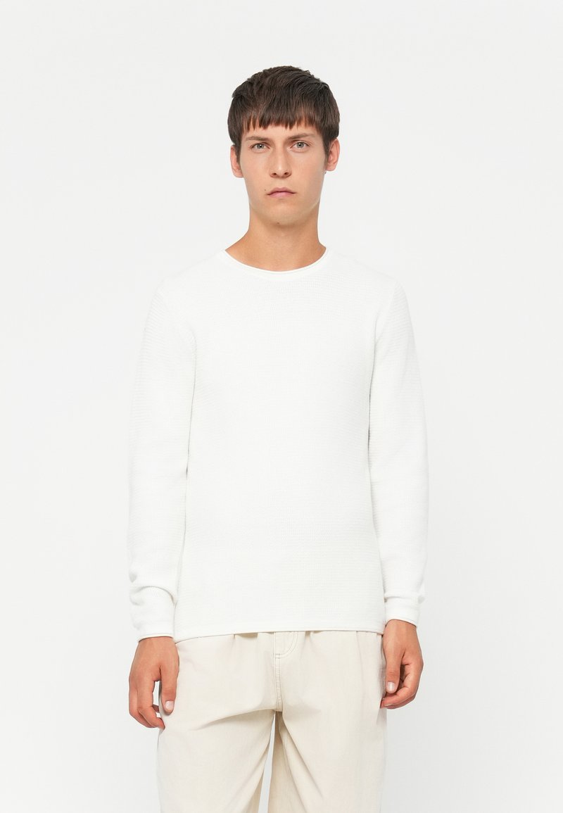 Witte, lange mouwen textuurtrui met een ronde hals, gecombineerd met lichtgekleurde, losvallende broek. Eenvoudig ontwerp, zonder zichtbare patronen of accenten.