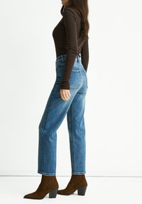 High-waisted blue denim jeans with a straight leg fit, paired with a fitted brown long-sleeve top and brown heeled ankle boots.