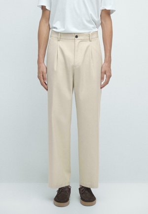Beige pleated trousers made of soft fabric, featuring a button closure, side pockets, and a relaxed fit. Paired with dark brown shoes.