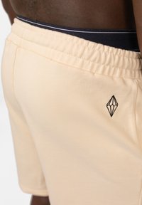 Licht perzikkleurige shorts met een elastische tailleband en een marineblauwe accent. Bevat een zwart diamantlogo geborduurd aan de linkerkant.