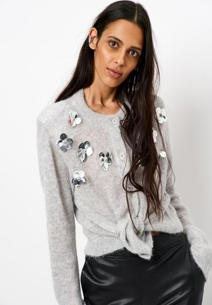 Cardigan en tricot gris clair avec des applications florales en sequins, un col rond, des boutons à l'avant et un nœud à la taille.