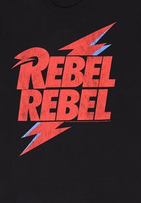 Sort t-shirt med fed rød og blå grafisk tekst, der læser "REBEL REBEL" med lynbolt detaljer og en slidt tekstur.