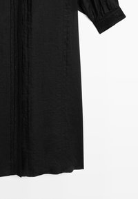 Black long-sleeve garment with button-down front and decorative stitching on the visible sleeve cuff and front panel.