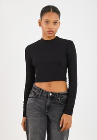 Crni rebrasti dugi crop top s visokim ovratnikom, uparen s izblijedjelim crnim trapericama koje imaju vidljivu kopču i prednje džepove.