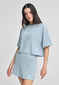Maglietta cropped azzurro chiaro con maniche corte, caratterizzata da un logo ricamato, abbinata a pantaloni corti azzurro chiaro con cintura elastica.