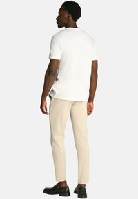 T-shirt bianco a maniche corte, vestibilità rilassata, abbinato a chinos beige slim-fit e scarpe slip-on nere; texture liscia e design semplice.