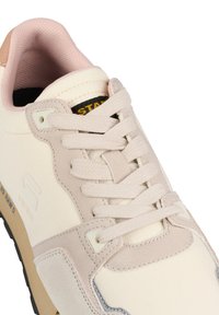 Baskets avec une tige en toile beige et crème, des accents rose pâle, des lacets texturés et un logo noir et jaune sur la languette.