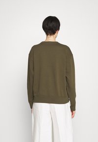 Olivgrön sweatshirt med klassisk rund halsringning, sänkt axelsöm, ribbade ärmslut och nederkant. Mjukt, texturerat tyg med en avslappnad passform.
