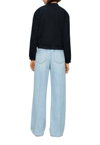 Sweatshirt noir avec ourlet et manches côtelés, associé à un jean large bleu clair avec poches arrière et une texture délavée.