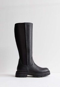 Botas negras hasta la rodilla hechas de material sintético suave, con suela gruesa con un patrón de revestimiento y elástico lateral para facilitar su uso.