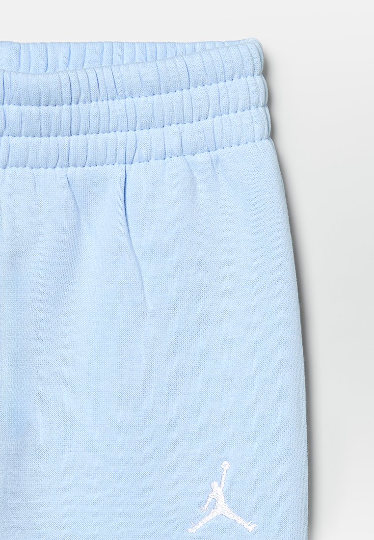 Pantalons de jogging bleu clair avec une taille élastique et un tissu texturé. Présente un logo brodé blanc sur la jambe inférieure.