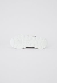 Sneakersåle med en teksturert hvit gummiyttersåle, med dype groper for grep og en lett buet form ved tåområdet.
