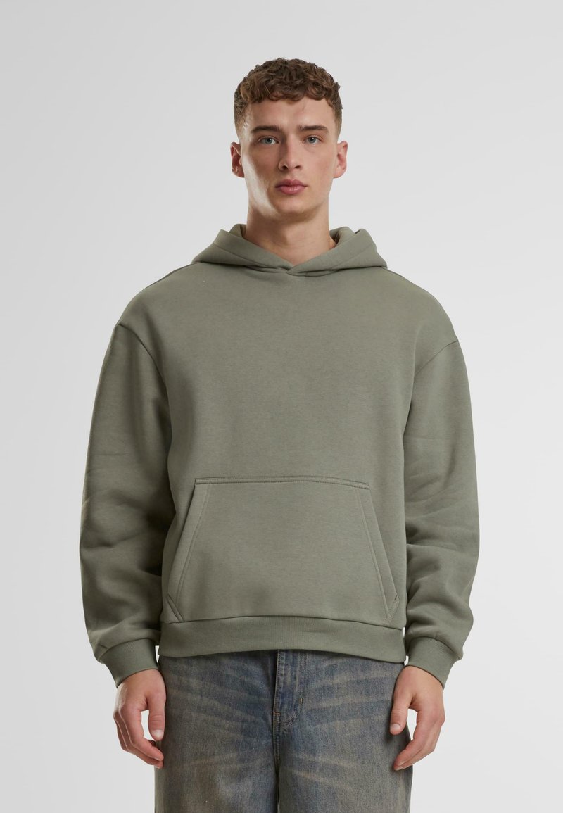 Sudadera con capucha en verde oliva, fabricada en un tejido suave. Presenta un bolsillo frontal tipo canguro y puños acanalados, ofreciendo un ajuste relajado.