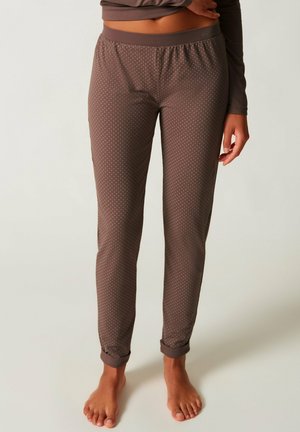 Brown slim-fit pajama pants with small white dots worn by a barefoot person standing against a plain background.
