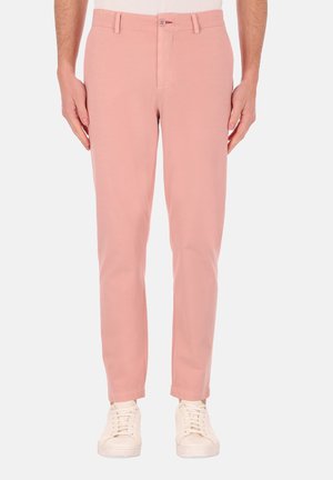 Pantaloni in tessuto rosa chiaro con una texture liscia, design affusolato, chiusura frontale con bottone e due tasche laterali, abbinati a sneakers bianche.