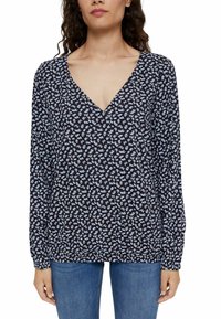 Donna che indossa una blusa blu navy con piccolo motivo floreale azzurro, scollatura a V, maniche lunghe, abbinata a jeans blu.