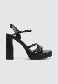 Sandalias de plataforma negras con un upper sintético texturizado, que presenta tres tiras anchas y una correa con hebilla en el tobillo, sostenidas por un tacón grueso.