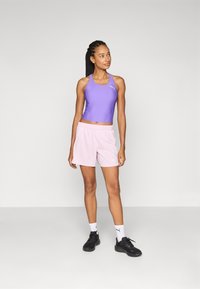 Lilla atletisk crop top og lyserøde shorts, laget av lett materiale, paret med svarte joggesko og hvite sokker med logo.