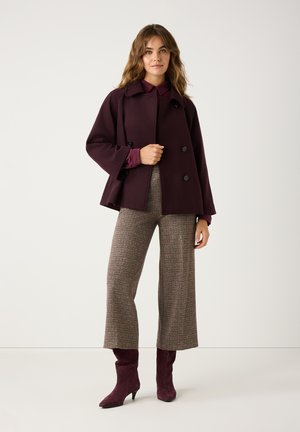 Burgundy double-breasted coat with two side pockets, paired with brown plaid wide-leg trousers and burgundy heeled ankle boots.