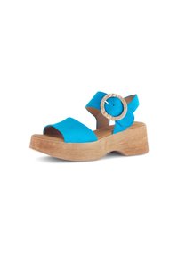 Blauwe suède open teen sandaal met een ronde houten plateauzool en een accentueerde cirkelvormige gesp op de enkelriem.