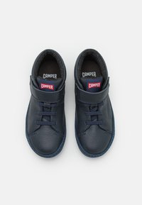 Pár navy modrých kožených bot Camper s tkaničkami a suchým zipem, zobrazené zeshora na bílém pozadí.