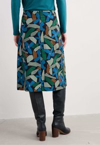 O fustă de lungime medie cu un model abstract multicolor, prezintă forme verzi, albastre, maroniu și roz, purtată cu cizme negre din piele până la genunchi.