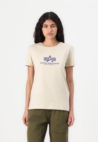 Bežinis medvilninis T-marškinėliai trumpomis rankovėmis, su purpuriniu grafiniu logotipu "ALPHA INDUSTRIES" ir trikampio dizainu priekyje.