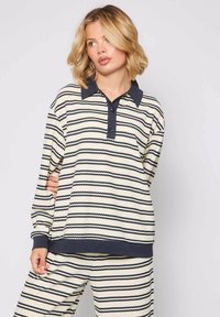 Jasno kremowa koszula polo z długim rękawem, w niebieskie zygzaki, z kontrastowym kołnierzykiem i listwą guzikową, połączona z pasującymi spodniami.