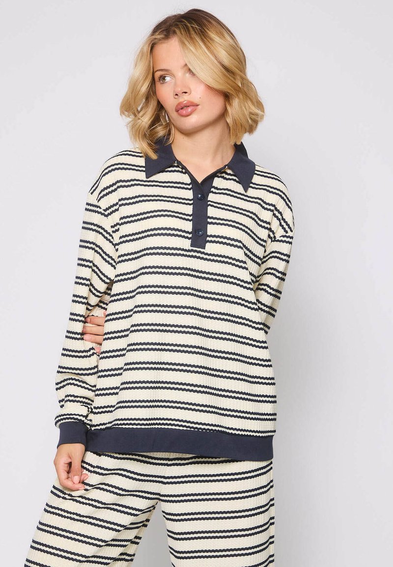 Jasno kremowa koszula polo z długim rękawem, w niebieskie zygzaki, z kontrastowym kołnierzykiem i listwą guzikową, połączona z pasującymi spodniami.