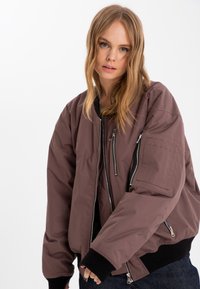 Isolerad bomberjacka i mauve med dragkedja fram, ribbad mudd och två sidofickor med dragkedja. Har en texturerad ficka på ärmen.