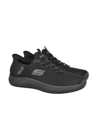 Zapatillas deportivas negras con parte superior de malla, suela flexible y diseño de cordones. Logo visible en el lateral y suela texturizada para agarre.