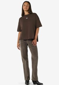 Brūna īsajām piedurknēm pārteikta t-krekls ar nelielu logotipa detaļu, apakšā valkāti teksturēti tumši brūni korduroja bikses un melnas papēžu potīšu zābaki.